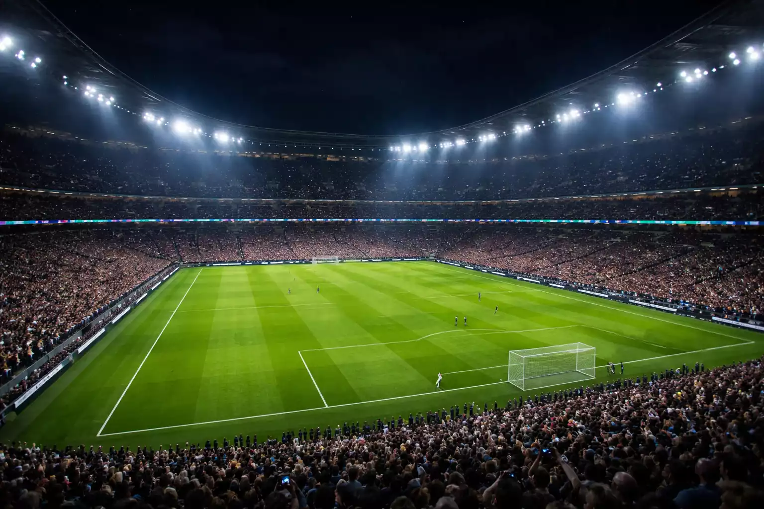 Estadio de fútbol inglés iluminado durante un partido nocturno de Premier League